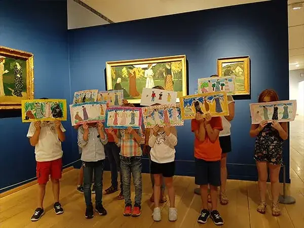 Photo d'enfants montrant leurs propositions de dessins en comparaison avec l'œuvre derrière eux